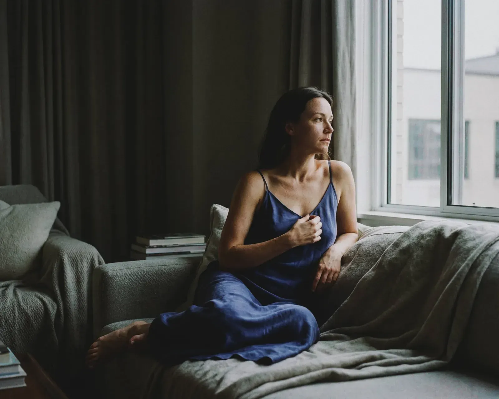 Mujer sentada en sillón azul mirando por la ventana, sesión boudoir íntima luz tarde