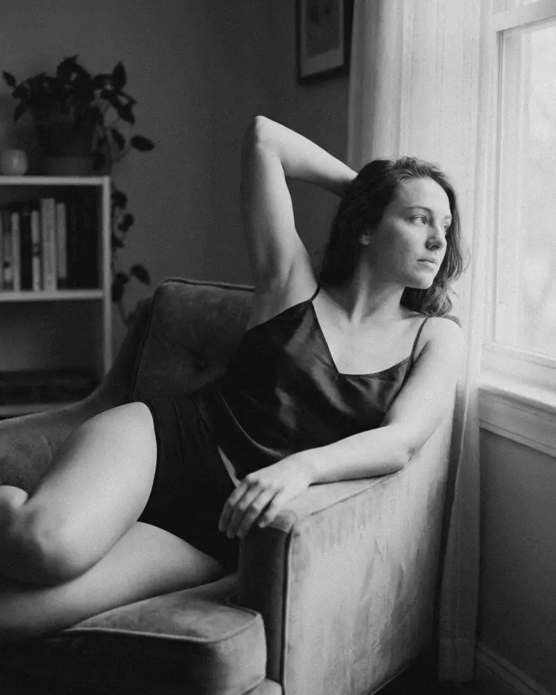 Pose recargada en sillón con brazo elevado en blanco y negro, fotografía boudoir