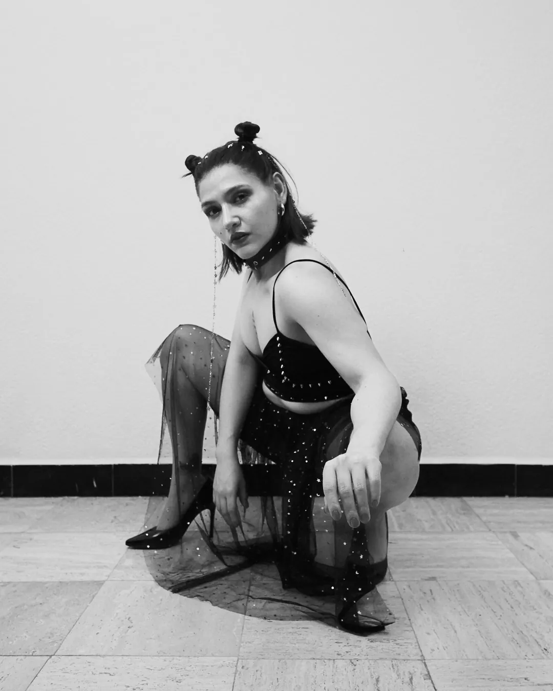 Mujer en cuclillas sobre falda de tul con mirada frontal, boudoir de estudio en blanco y negro