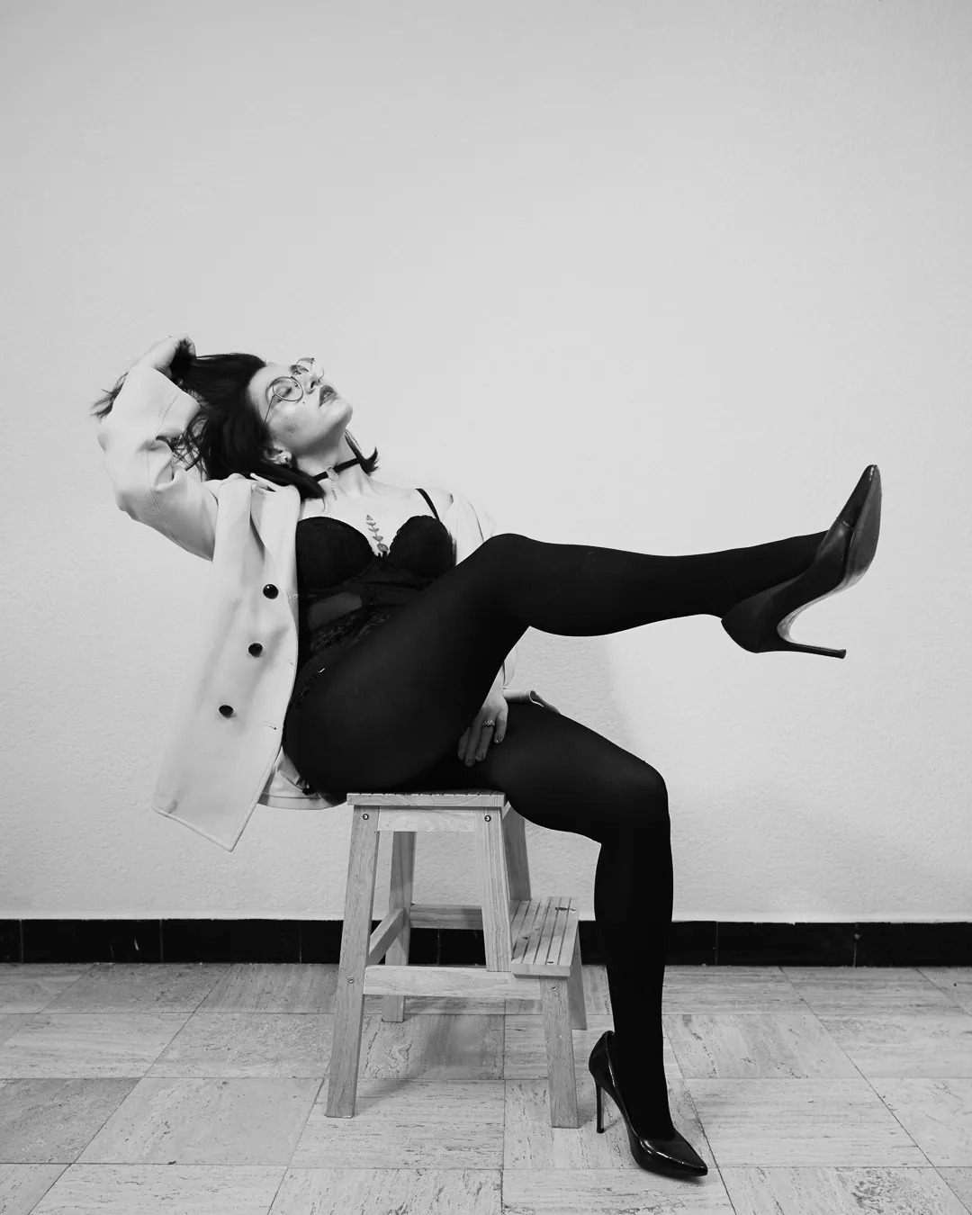 Mujer recostada sobre banco con pierna extendida y tacones, fotografía boudoir de estudio en blanco y negro