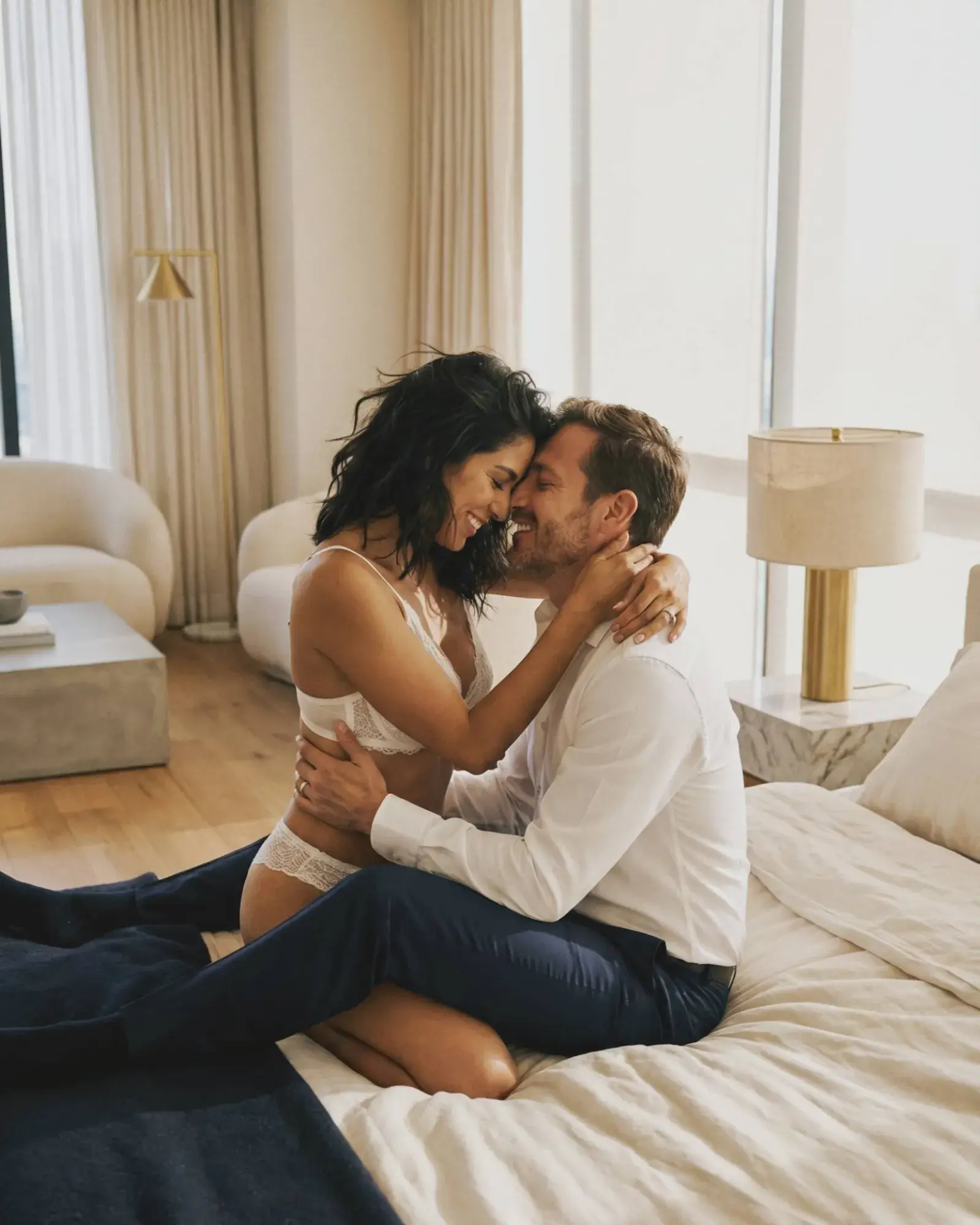 Pareja nupcial boudoir besándose en sillón con velo y lencería, sesión íntima