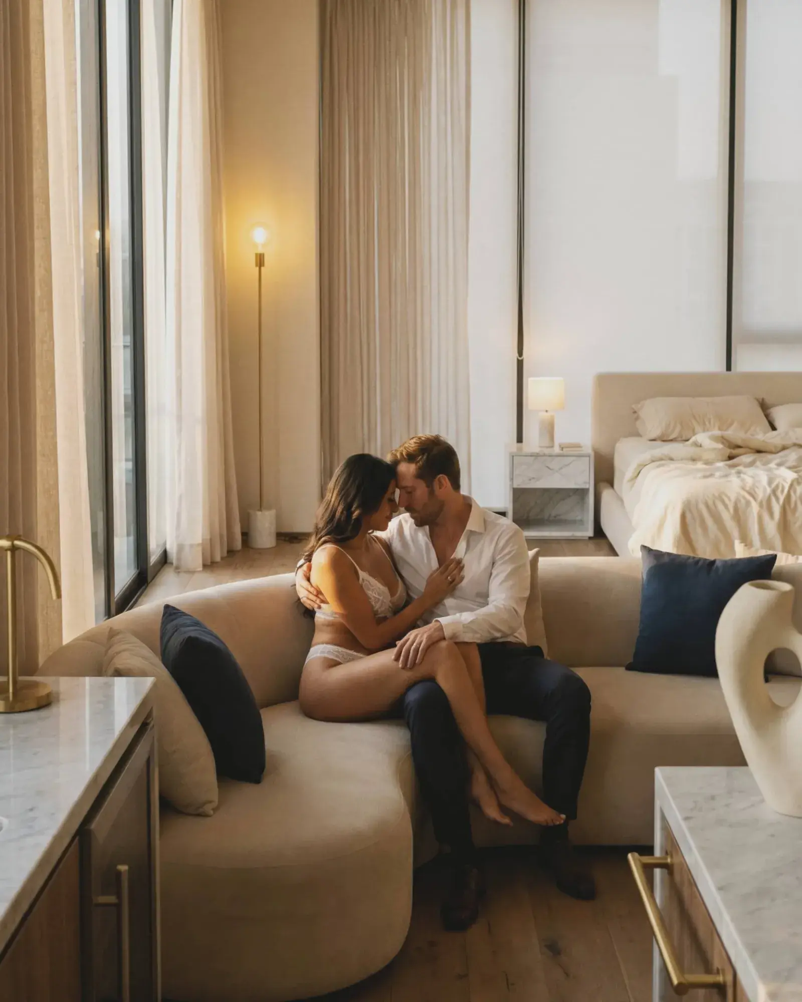 Pareja nupcial boudoir abrazados en sillón con luz natural cálida